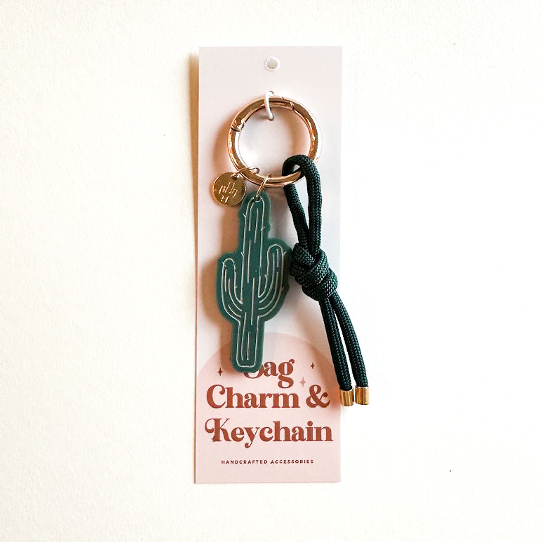 Miminoo handcrafted Saguaro Cactus Bag Charm & Keychain featuring a dark green acrylic cactus with white etched details, a gold-accented keyring, a small gold cactus charm, and a dark green knotted cord with gold tips, on a display card