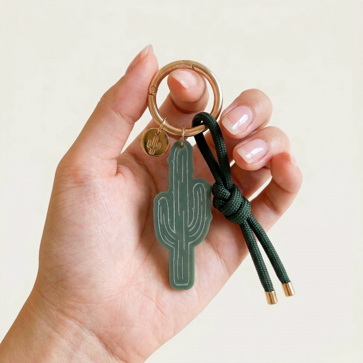 Hand holding a cactus bag charm keychain with a cactus design on a beige background